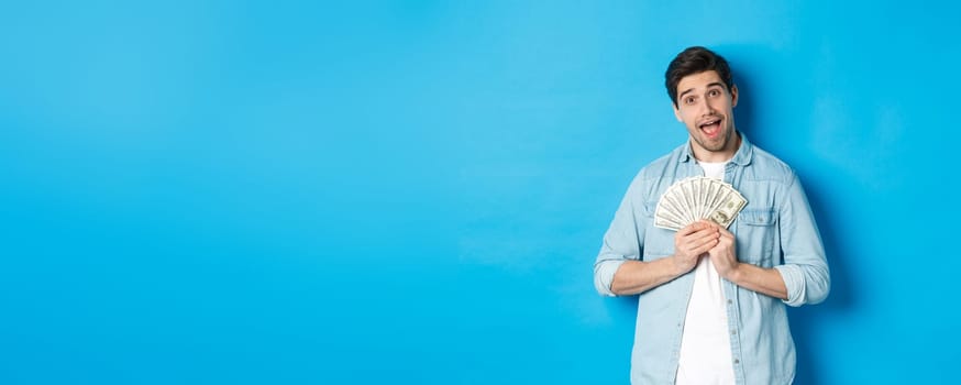 Smiling greedy guy hugging money and smiling, unwilling to share, standing over blue background.