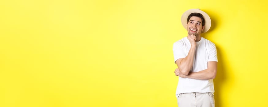 Young thoughtful man tourist imaging something, looking at upper left corner and smiling, thinking and standing over yellow background.