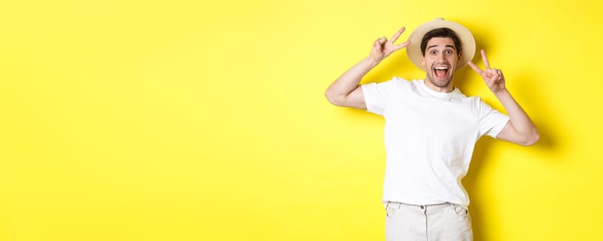 Concept of tourism and vacation. Happy male tourist posing for photo with peace signs, smiling excited, standing against yellow background.