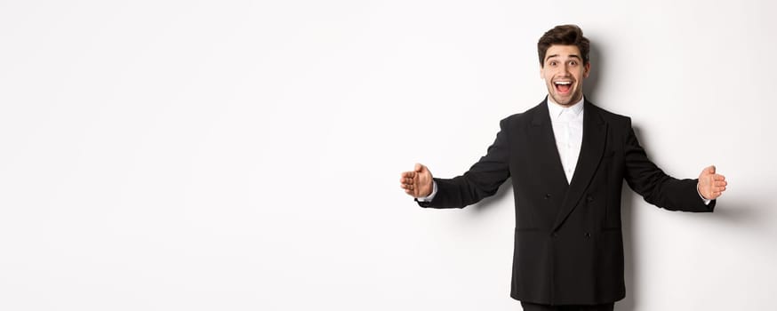 Portrait of excited handsome man in suit, shaping big object on copy space and smiling amazed, holding something, standing over white background.