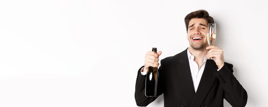 Close-up of handsome drunk guy in suit, holding glass of champagne and celebrating new year, standing over white background.