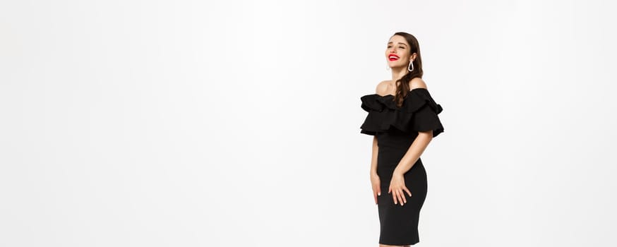 Vertical view of beautiful young woman in luxurious dress, red lips and jewelry, standing with christmas gifts on white background, standing over white background.