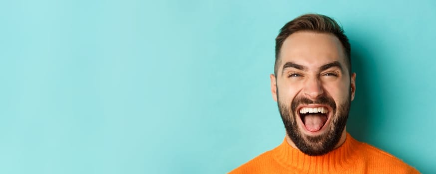 Headshot of happy and carefree man with beard, laughing and looking at camera, standing in orange sweater.