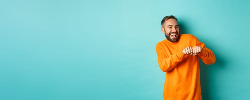 Happy man dancing and celebrating success, feeling like winner, smiling and rejoicing, light blue background.