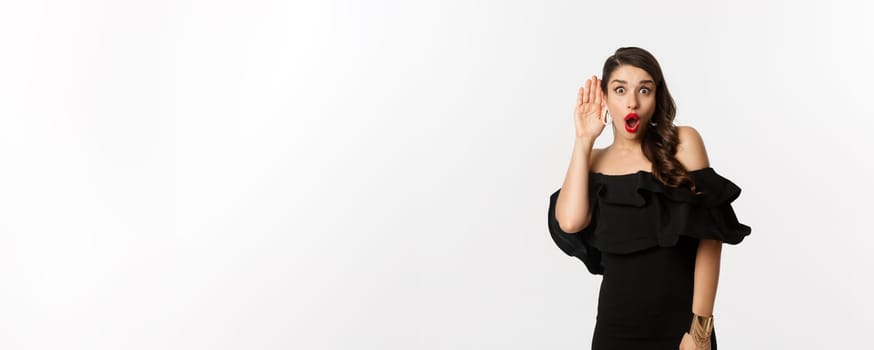 Fashion and beauty. Image of excited woman eavesdropping, holding hand near ear and leaning left to hear gossips, white background.