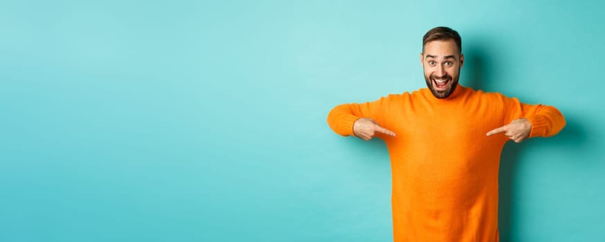 Happy man pointing at sweater, showing your logo banner on clothes, standing over light blue background.