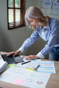 Portrait of a thoughtful Asian businesswoman looking at financial statements and making marketing plans using a computer on her desk.