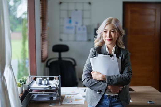 Portrait of a woman business owner showing a happy smiling face as he has successfully invested her business using computers and financial budget documents at work.