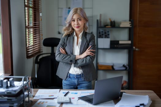 Portrait of a woman business owner showing a happy smiling face as he has successfully invested her business using computers and financial budget documents at work.