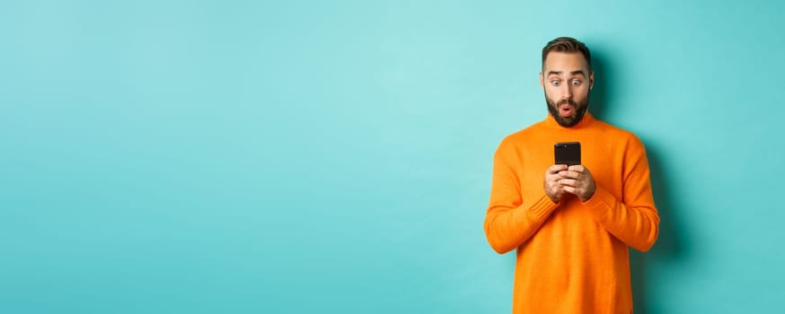 Image of man reading message with surprised face, standing amazed over light blue background.