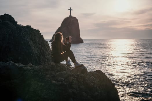 Woman travel sea. Happy tourist taking picture outdoors for memories. Woman traveler looks at the edge of the cliff on the sea bay of mountains, sharing travel adventure journey.