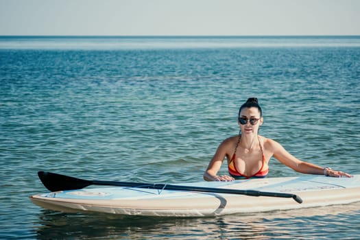Sea woman sup. Silhouette of happy middle aged woman in rainbow bikini, surfing on SUP board, confident paddling through water surface. Idyllic sunset. Active lifestyle at sea or river