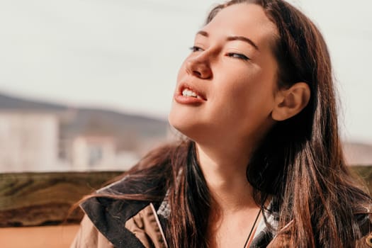 Happy young smiling woman with freckles outdoors portrait. Soft sunny colors. Outdoor close-up portrait of a young brunette woman and looking to the camera, posing against nature background.