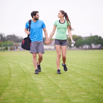 Taking the field together. a young couple in exercise gear walking hand in hand on a sports field