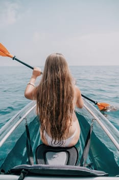 Woman in kayak back view. Happy young woman with long hair floating in transparent kayak on the crystal clear sea. Summer holiday vacation and cheerful female people having fun on the boat.