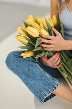 Cute smiling girl with a bouquet of yellow tulips in the interior.