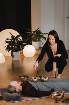 A young beautiful woman is doing a massage with singing bowls and a koshi bell to another girl. Sound therapy.