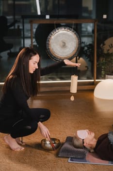 A young beautiful woman is doing a massage with singing bowls and a koshi bell to another girl. Sound therapy.