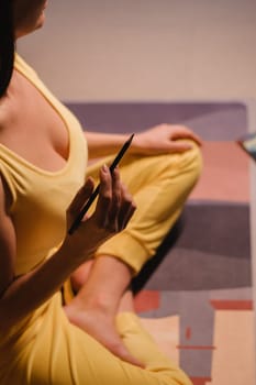 A girl in yellow clothes sitting on the floor holding pencils for drawing.