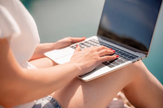 Freelance women sea working on the computer. Good looking middle aged woman typing on a laptop keyboard outdoors with a beautiful sea view. The concept of remote work