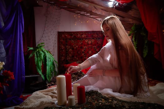 Beautiful arabian girl with candles in red room full of rich fabrics and carpets in sultan harem. Photo shoot of woman an oriental style odalisque. Model poses in sari as caring wife and hostess