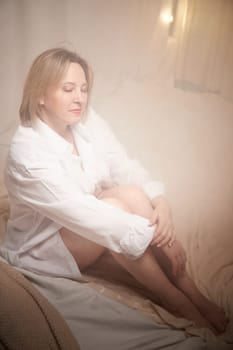 Portrait of sexual body positive adult lady woman in intimate in tender space indoors in a bedroom. Plump girl poses in black underwear and white shirt during boudoir style photo shoot