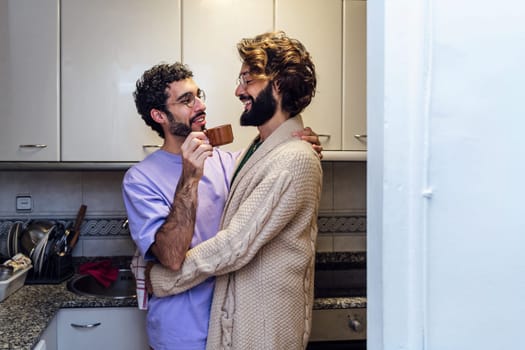 gay male couple hugging affectionately while having morning coffee in the kitchen, concept of home lifestyle and love between people of the same sex, copy space for text