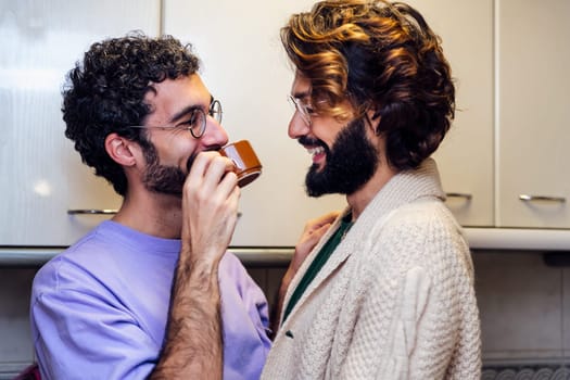 gay male couple smiling affectionately while having morning coffee in the kitchen, concept of home lifestyle and love between people of the same sex