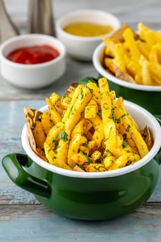 Golden French Fries in an enamel bowl with various sauces on the side