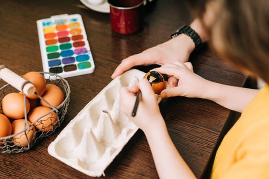 Easter day. Male Father and son painting eggs on wooden background. Family sitting in a kitchen. Preparing for Easter, creative homemade decoration. Child kid boy having fun and painting easter eggs