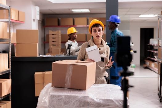 Retail storehouse worker recording smartphone video with goods unpacking. Young warehouse employee explaining stock supply management and order packing on mobile phone camera