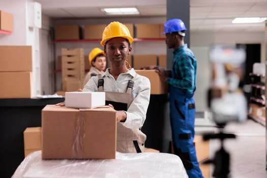 African american warehouse operator managing parcels receiving portrait. Industrial storehouse manager preparing freight cardboard boxes for export transportation and looking at camera