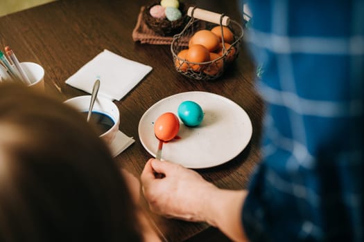 Easter day. Male Father and son painting eggs on wooden background. Family sitting in a kitchen. Preparing for Easter, creative homemade decoration. Child kid boy having fun and painting easter eggs