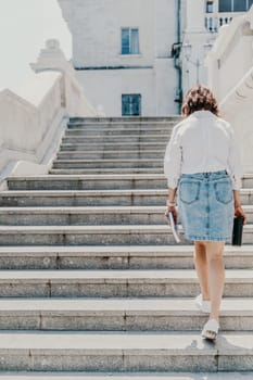 Woman staircase city. A business woman in a white shirt and denim skirt walks down the steps of an ancient building in the city.