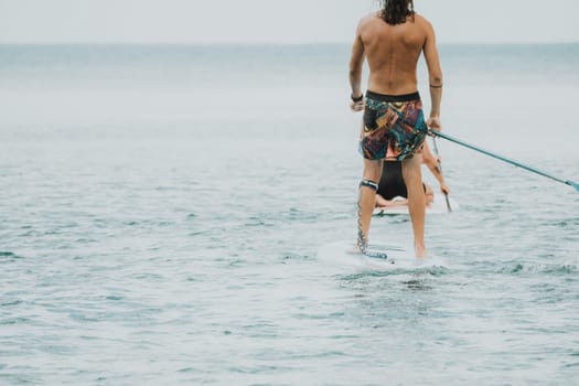 Sea woman and man on sup. Silhouette of happy young woman and man, surfing on SUP board, confident paddling through water surface. Idyllic sunset. Active lifestyle at sea or river