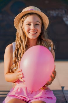 Portrait of a girl in a hat with a pink balloon. She is dressed in pink clothes and her hair is long and loose