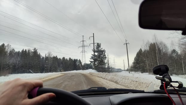 Hand of woman on the steering wheel in a car and forest and snow on the side of the road on a winter day. Woman driving car in winter travel in landscape with snow covered woods