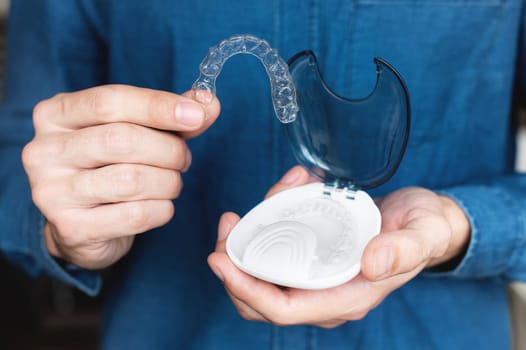 close-up of a young caucasian man holding an invisible dental retainer and a case for their storage and protection. beautiful teeth treatment course and banner advertising concept.