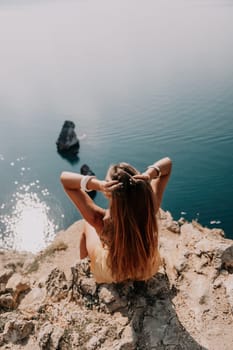 Woman travel sea. Happy tourist taking picture outdoors for memories. Woman traveler looks at the edge of the cliff on the sea bay of mountains, sharing travel adventure journey.