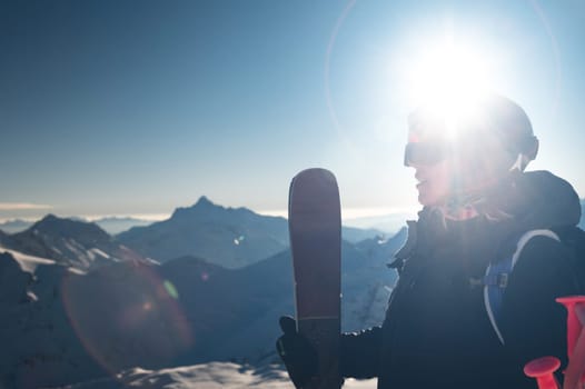 Young woman with skis near the hill against the backdrop of the sun's rays. Skier, skiing, winter sport, female skier portrait.