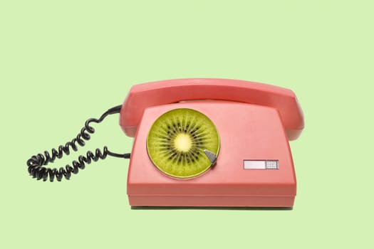 Playful retro phone with a disc of fruit kiwi. Stylish pop art concept about technology and fruits. High quality photo