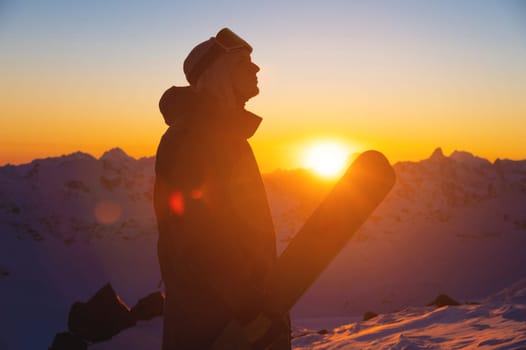 silhouette of a skier with skis standing on a slope at sunset against a mountain range. sportsman portrait.