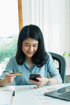 Portrait of young Asian woman using credit card and phone for online shopping.