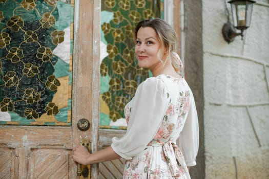 woman in a flower dress opens the door to the house.