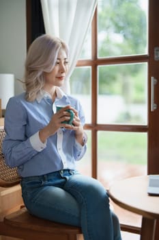 Portrait of an Asian business woman drinking coffee while working with a computer on her desk.