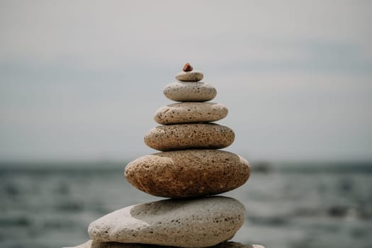 Pyramid stones on the seashore with warm sunset on the sea background. Happy holidays. Pebble beach, calm sea, travel destination. Concept of happy vacation on the sea, meditation, spa, calmness.