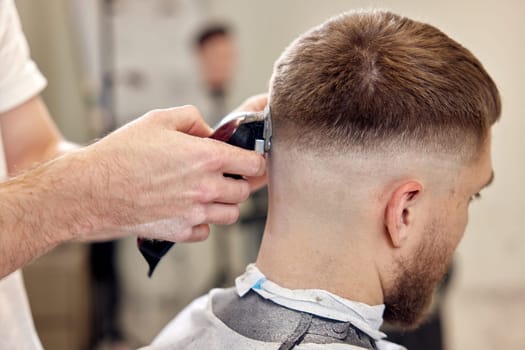 Barber trim hair with clipper on handsome bearded man in barber shop.