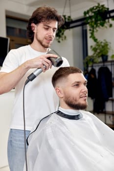 Professional hairdresser during work with man client with hair dryer in barber shop. Haircut in the barbershop.