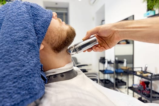 Barber shaving handsome bearded man in barber shop.