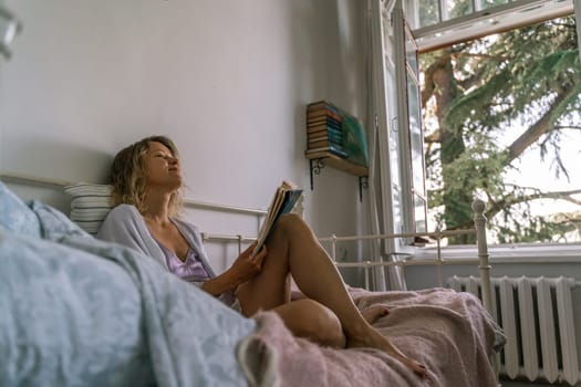 Girl reading a book in bed, lying on her stomach smiling happy and relaxed on a leisure day at home.